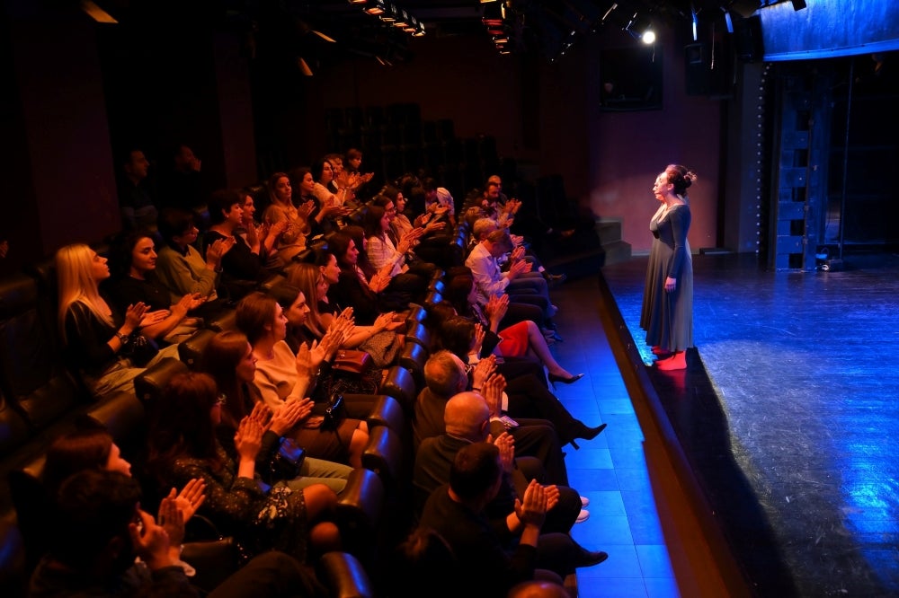 Audience applauding a performer on stage at a live theater event.