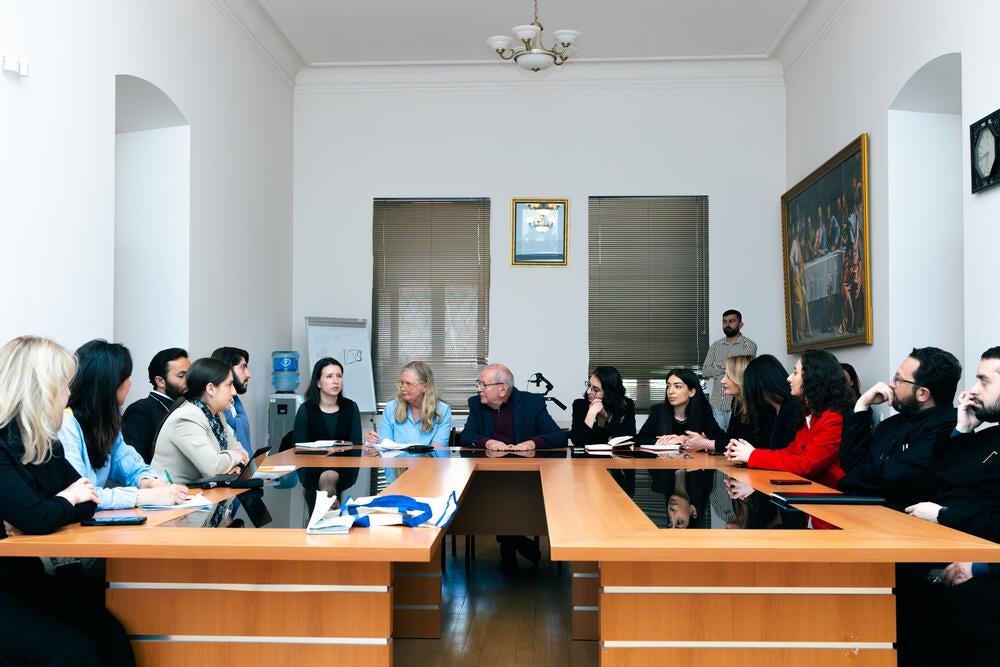 A group of professionals is gathered around a conference table in a well-lit meeting room, engaging in a discussion.