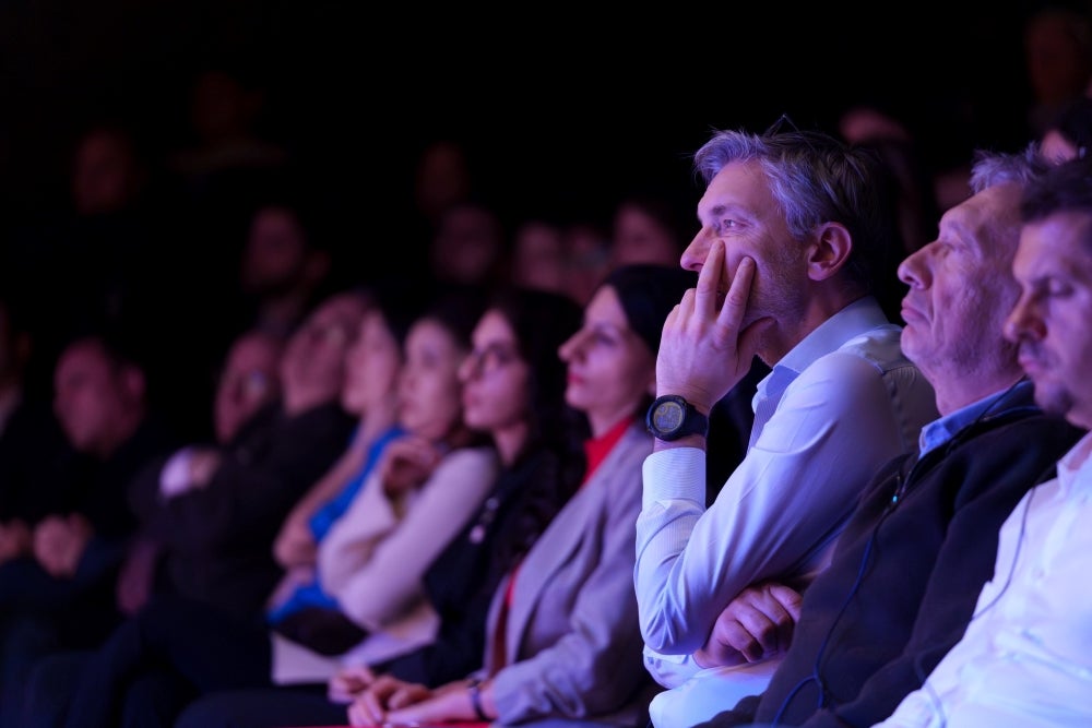 Audience members attentively watching a performance, with various expressions of engagement.