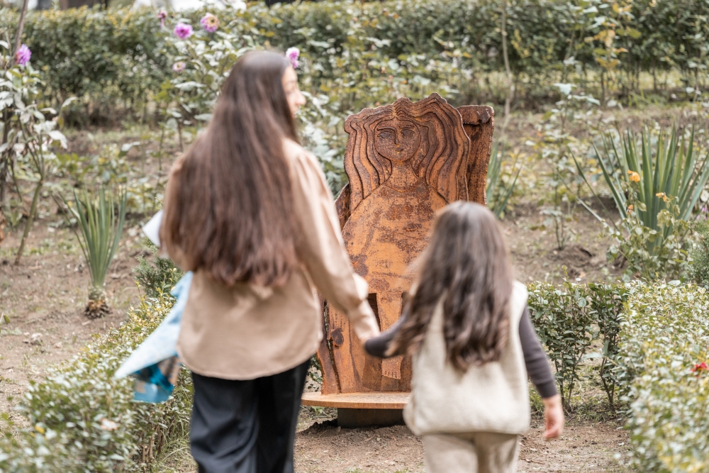 Two girls with long hair walking towards a large sculpture in a park.