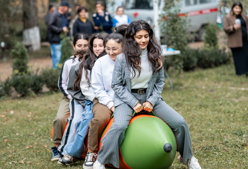 Four individuals laughing joyfully while sitting on colorful bouncing balls at an outdoor event.