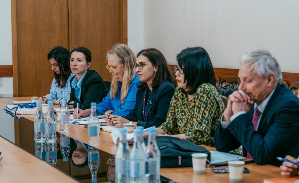 Group of professionals sitting at a conference table during a meeting, with water bottles and papers in front of them.