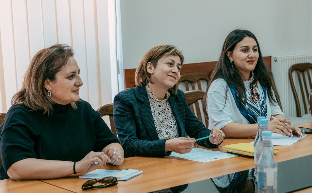 Three professionals seated at a table during a meeting, appearing engaged and attentive.