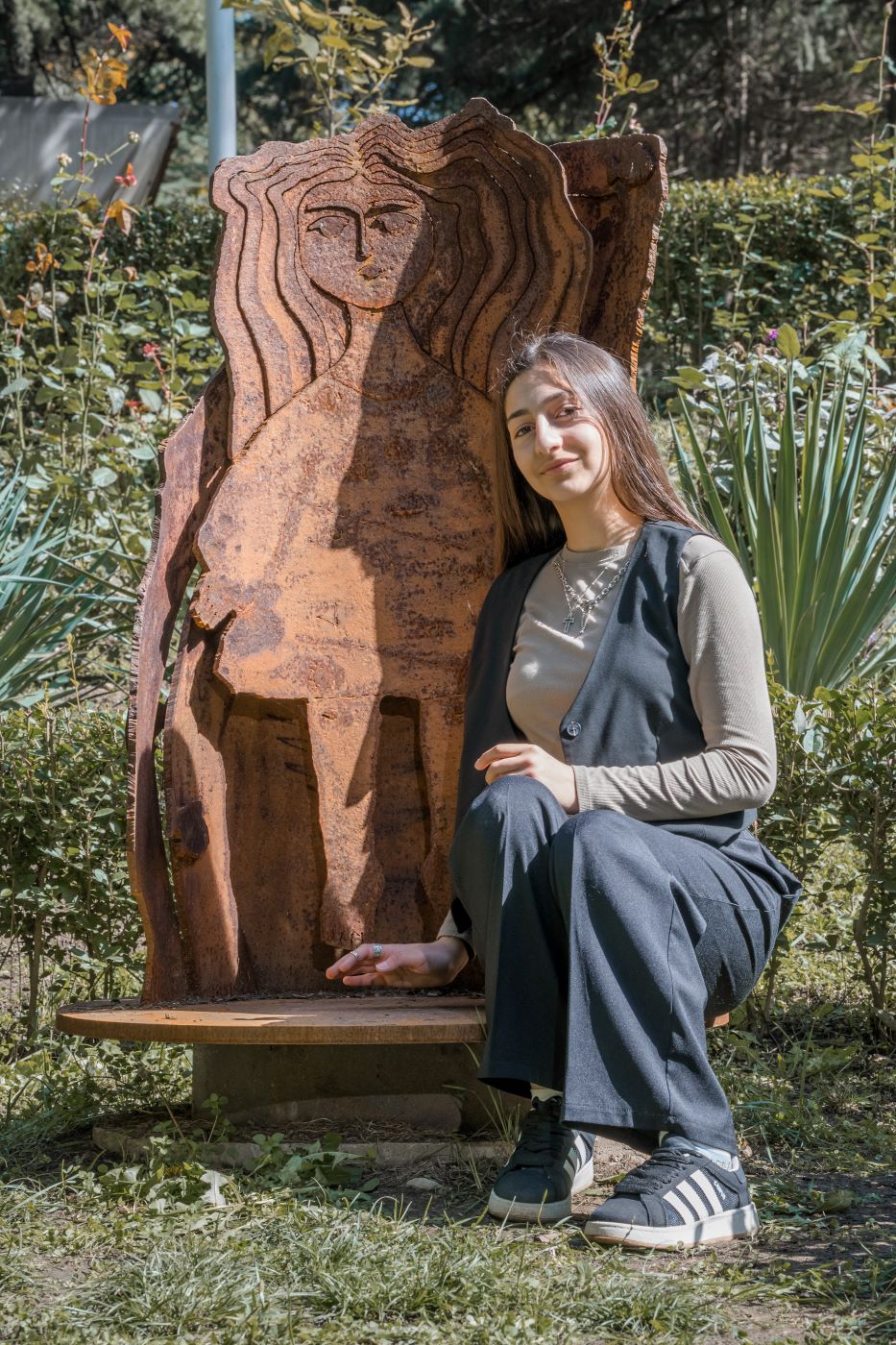 Neli, siting next to the NE's sculpture and looking at the camera.