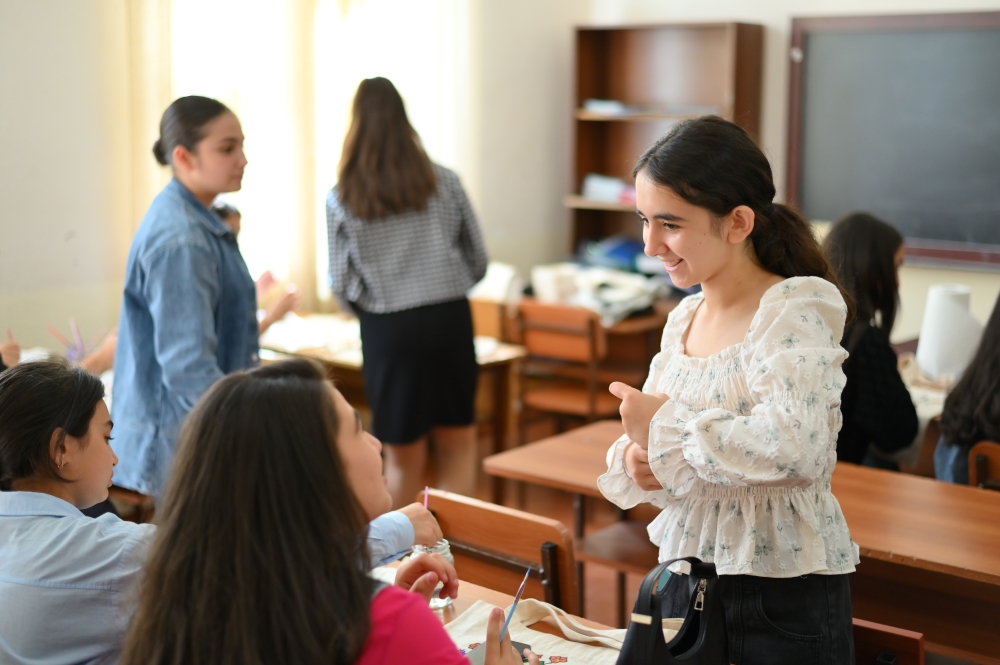 Students interacting in a classroom with one student smiling and others conversing in the background.