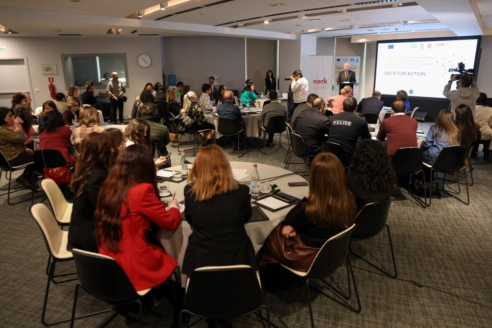 Attendees at a conference, focused on 'Data for Action', listening to a speaker at the front of a modern meeting room.