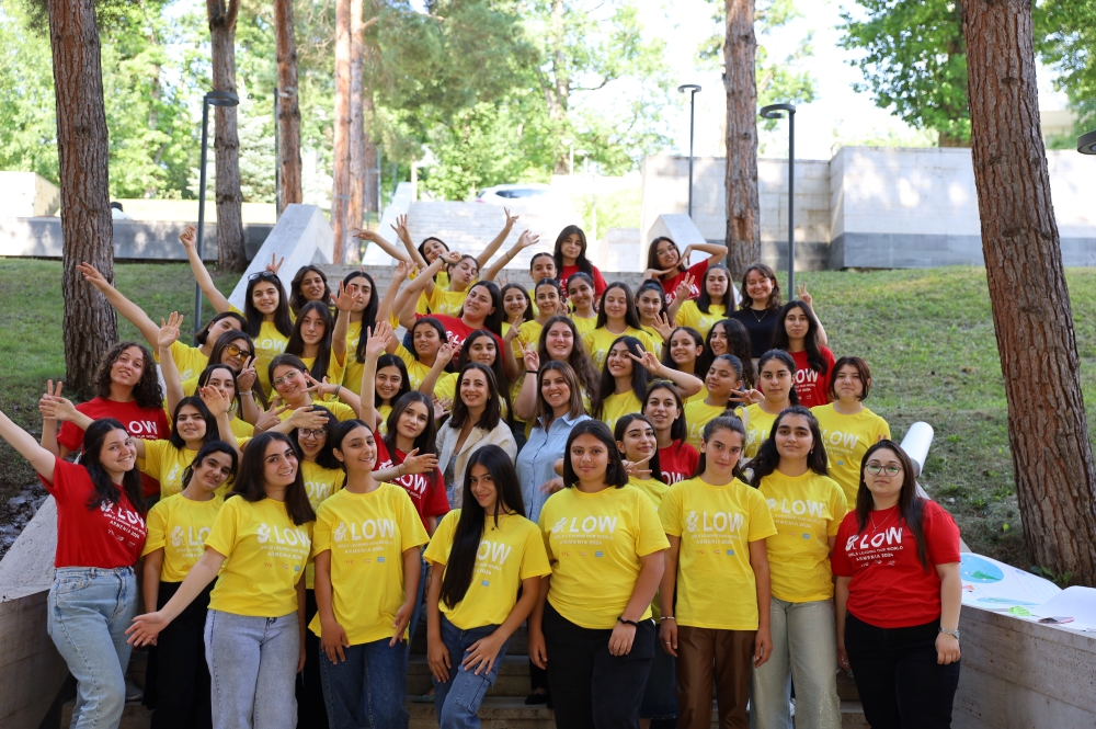  Group of individuals in red and yellow t-shirts with the word "GLOW" printed on them, posing cheerfully in an outdoor area surrounded by trees.