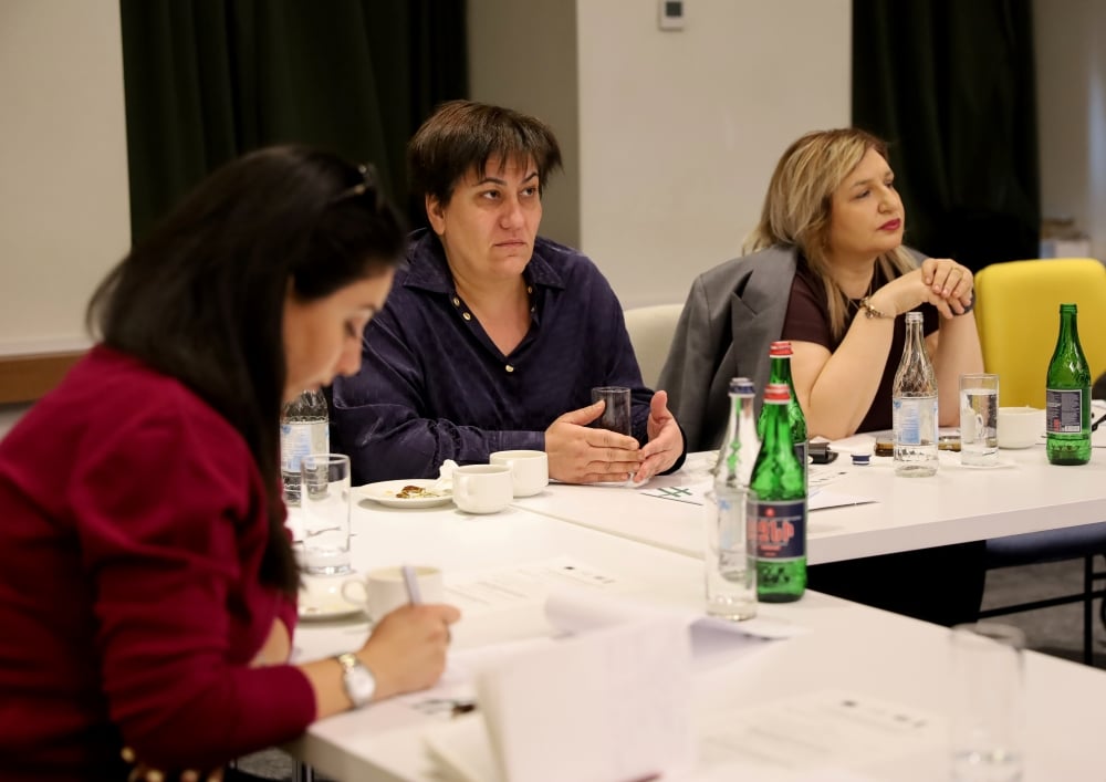 Three professionals are engaged in a discussion at a conference table, with papers in front of them.