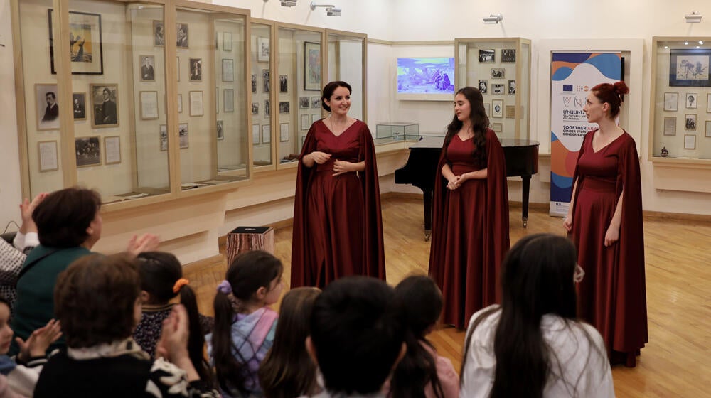 Three women - actresses playing the '100 years later' performance are singing on the stage.