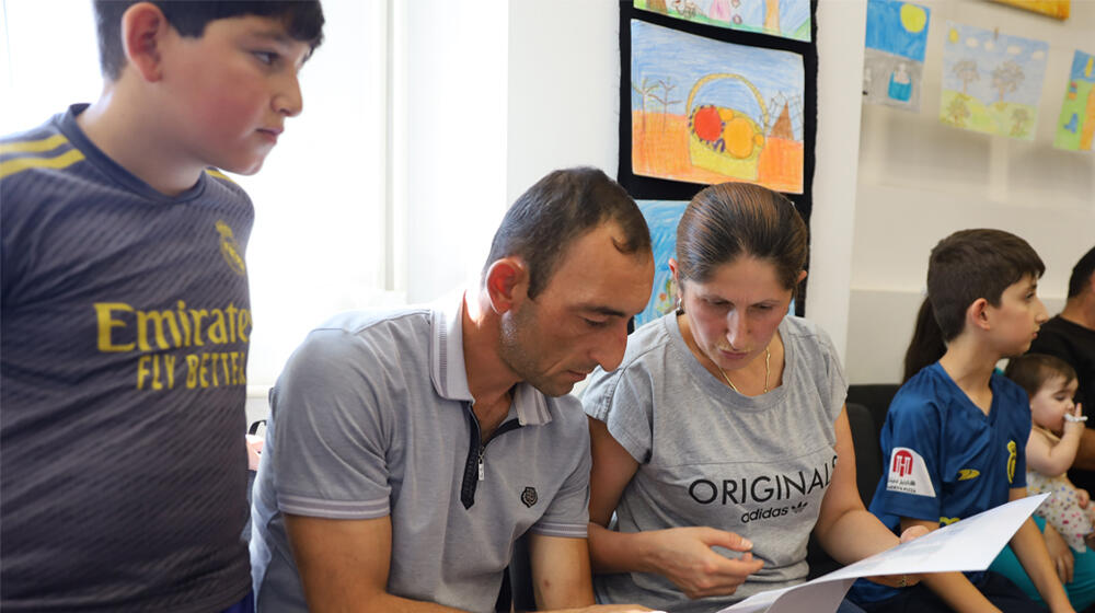 Image of a young Chichyan family with their children. The father and mother are reading a paper. 