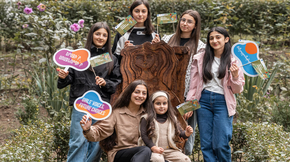 Group of six people posing with colorful placards in a park, expressing environmental awareness and girls empowerment.