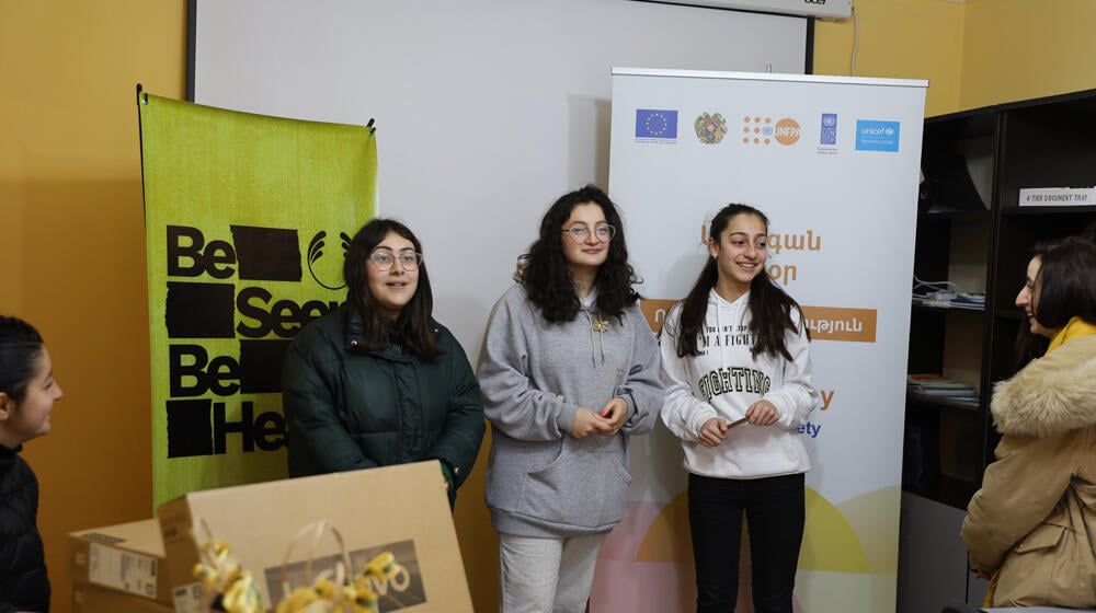 Three young girls from border communities of Tavush province standing together smiling in a room