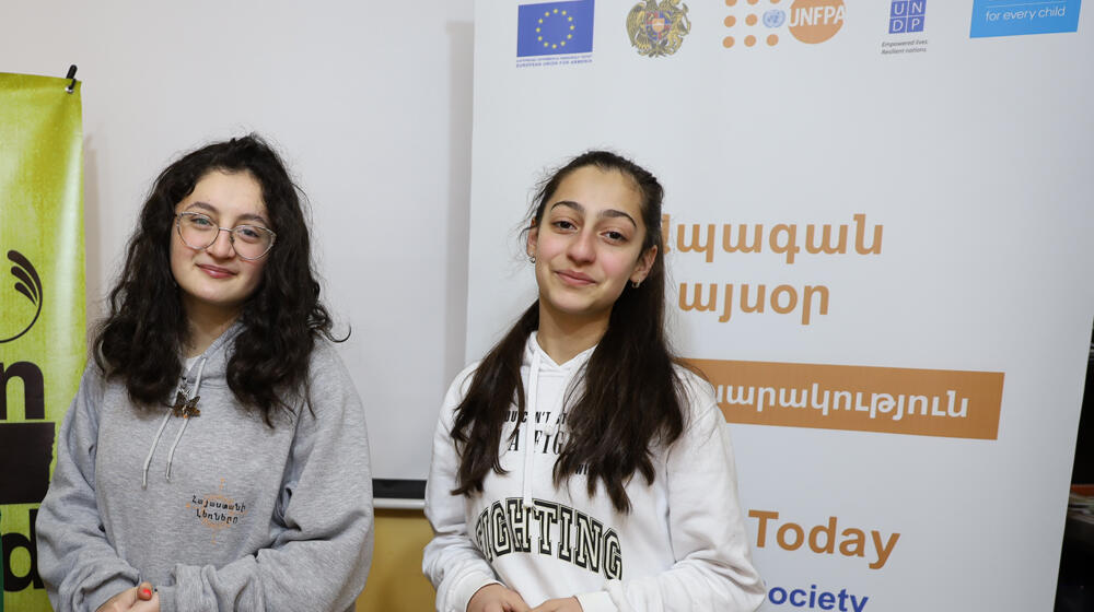 Two girls standing in front of a banner and smiling.